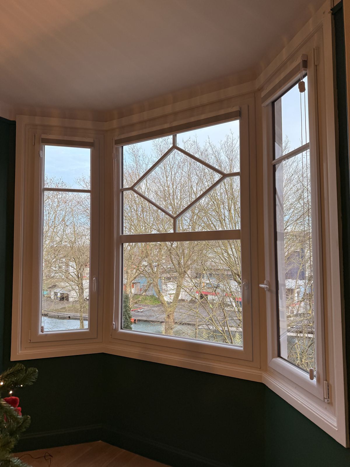 Bow-window en bois clair avec petits bois décoratifs, vue sur les arbres